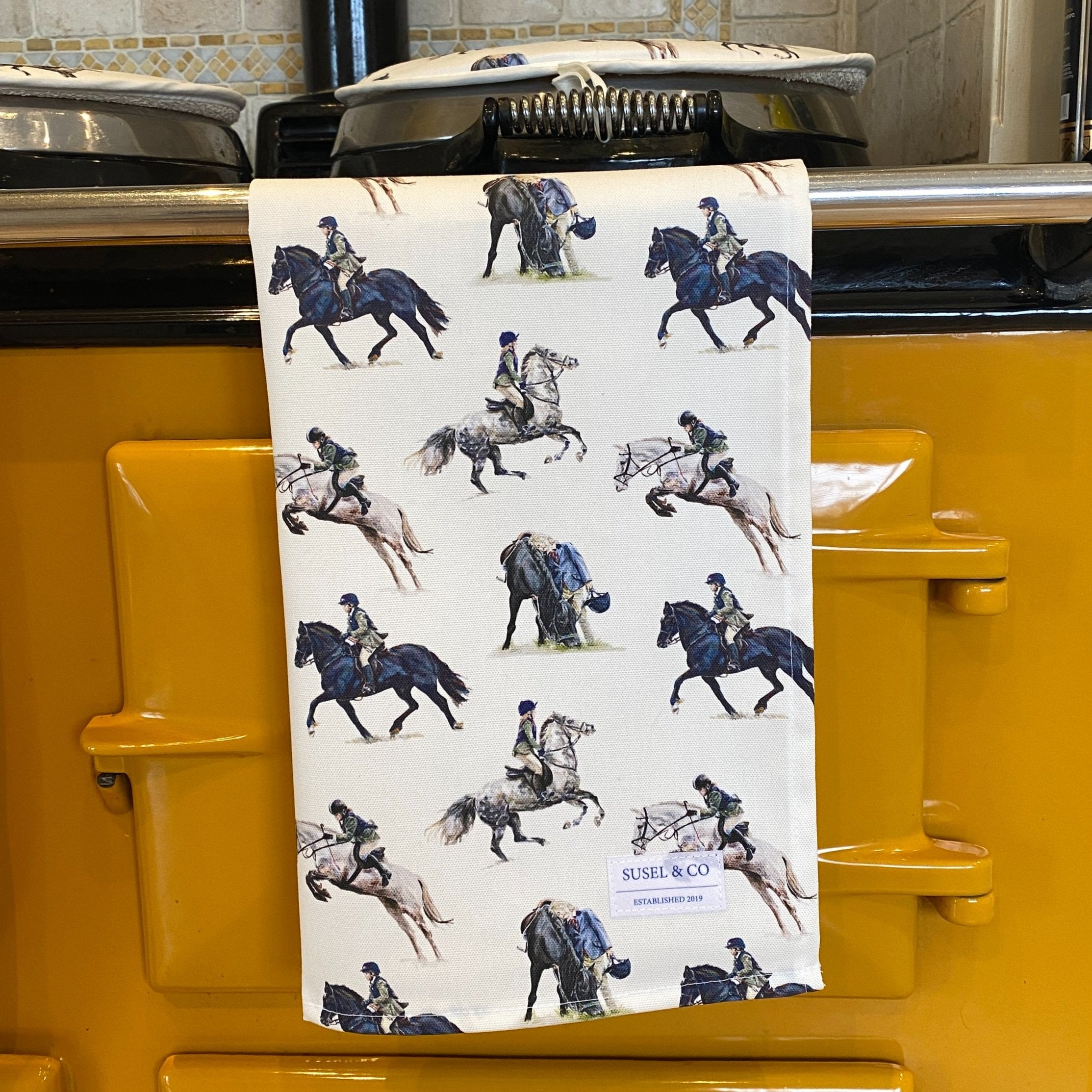 A tea towel with a horse and rider pattern hanging on a yellow oven.